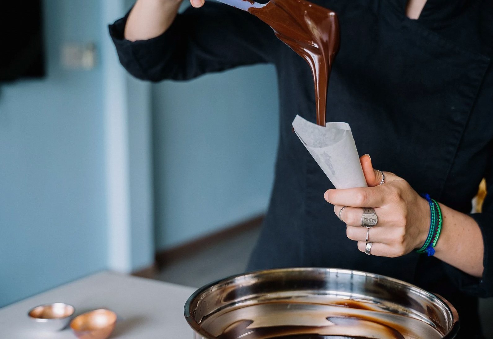 シェフがキッチンで食品の準備のために溶かしたチョコレートを絞り袋に注いでいる。